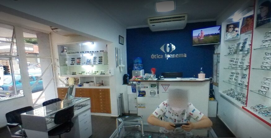 Interior da Ótica Ipanema: balcão de atendimento, vitrines de armações e a parede azul com o símbolo da marca
